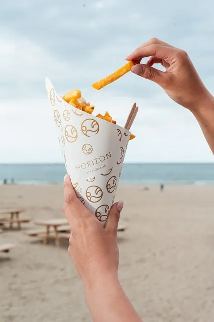 Friet in een bedrukte papieren puntzak op het strand